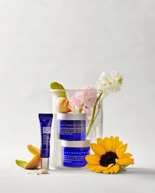 Naturopathica skincare products including serums and moisturizers displayed with white hyacinth and sunflower against a white background.
