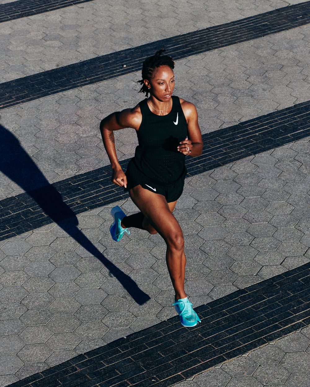 Athletic woman in running attire sprints across an urban landscape with geometric shadows and pavement details in an eye-level shot.