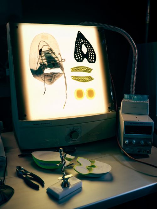 Product design of deconstructed shoe and elements on illuminated display stand. Components include sole, upper, and support pieces.