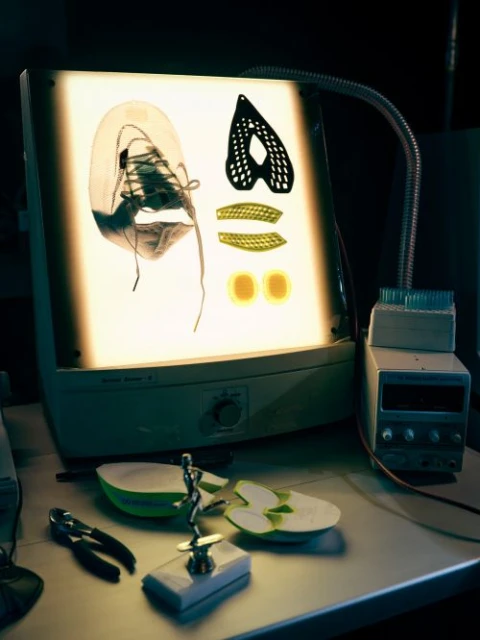 Product design of deconstructed shoe and elements on illuminated display stand. Components include sole, upper, and support pieces.