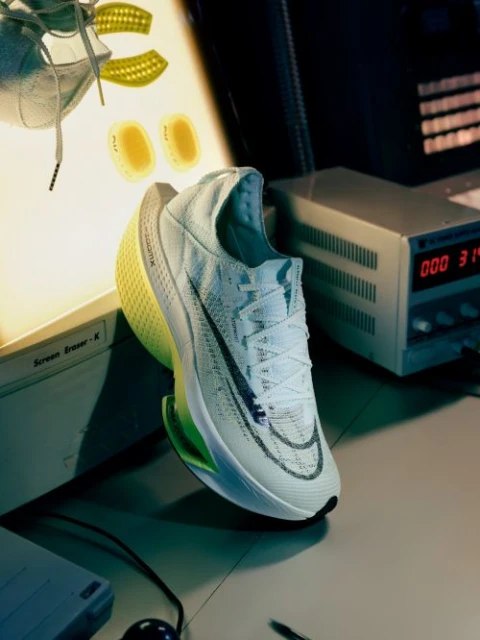 White Nike running shoe with bright yellow sole, floating near vintage computer equipment. Studio product shot, angled view.