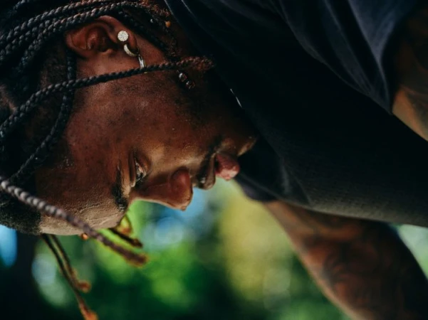 Close-up profile of a black man with braided hair, hoop earrings, and a dark t-shirt shot by Brian Kelley.