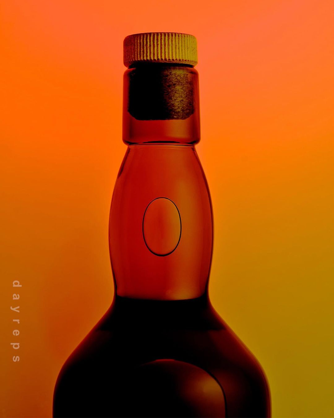 A glass bottle with a ribbed cap stands against a vivid orange and yellow gradient backdrop, its dark silhouette creating contrast.