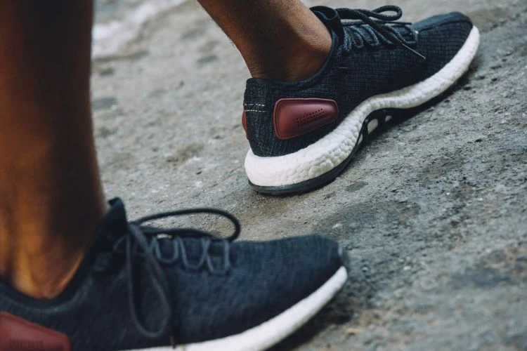 Close-up of feet in dark gray athletic sneakers with red accent, white soles, laces tied on a textured gray concrete surface.