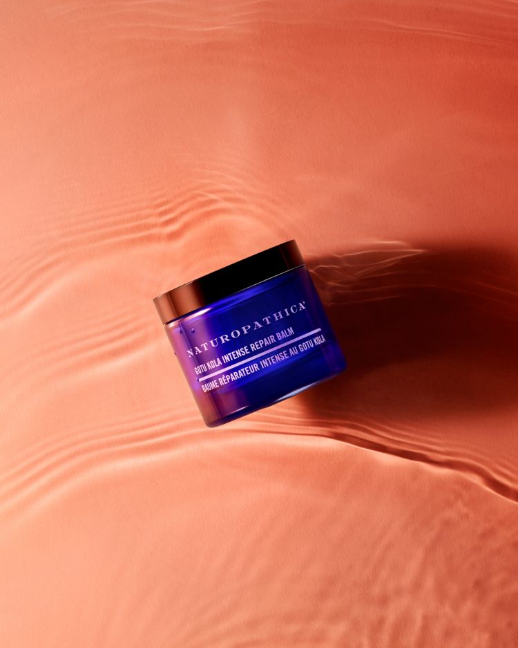 Studio shot of blue Naturpathica balm jar with black lid on peach background with water ripple effect. Beauty and skincare product.