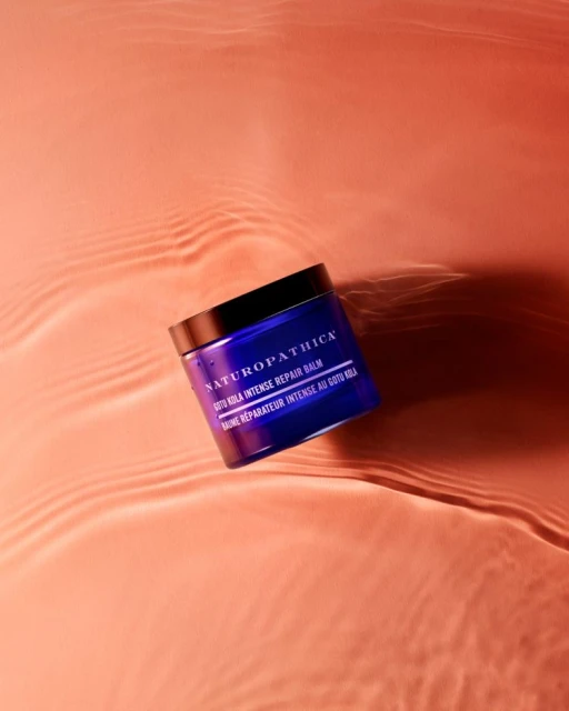 Studio shot of blue Naturpathica balm jar with black lid on peach background with water ripple effect. Beauty and skincare product.