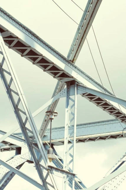 Detailed view of a steel truss bridge structure with an attached street lamp, showcasing complex geometric patterns against a light sky.