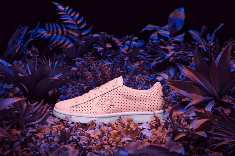 Perforated peach-colored Converse sneaker with a star logo, set among blue and purple leafy foliage against a dark background.