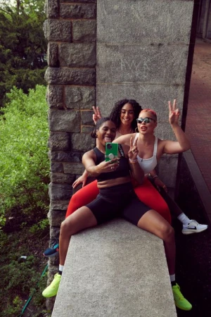 Three young women taking a selfie together while sitting on a concrete wall outdoors