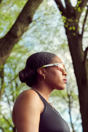 Black woman wearing sports sunglasses and a black athletic top outdoors against a backdrop of trees