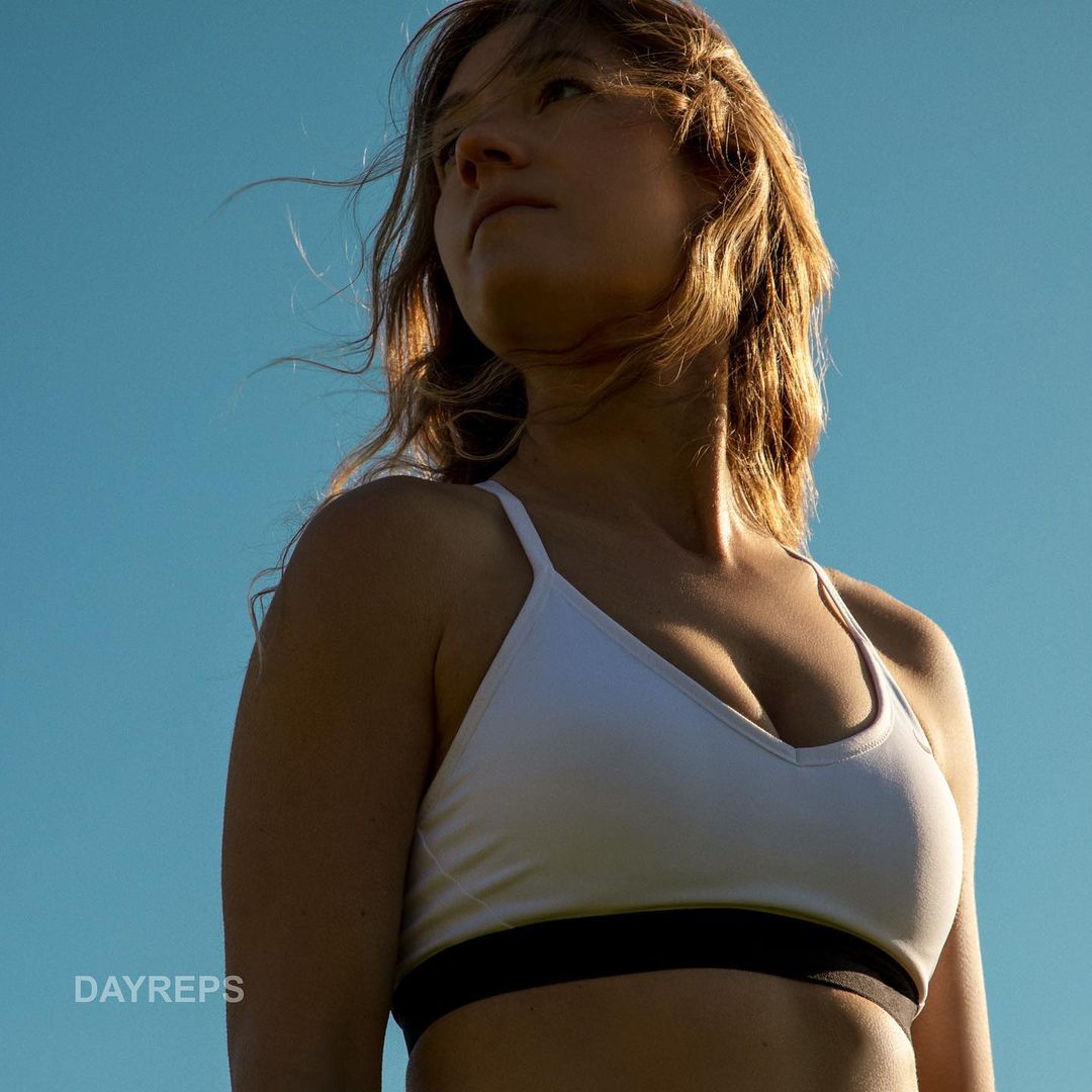 Young woman in a sports bra against a blue sky, looking upwards. Outdoor portrait shot.