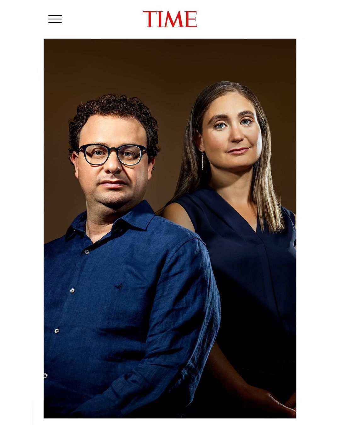 Portrait of a man wearing glasses and a blue shirt standing beside a woman against a dark studio background