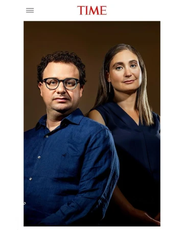 Portrait of a man wearing glasses and a blue shirt standing beside a woman against a dark studio background