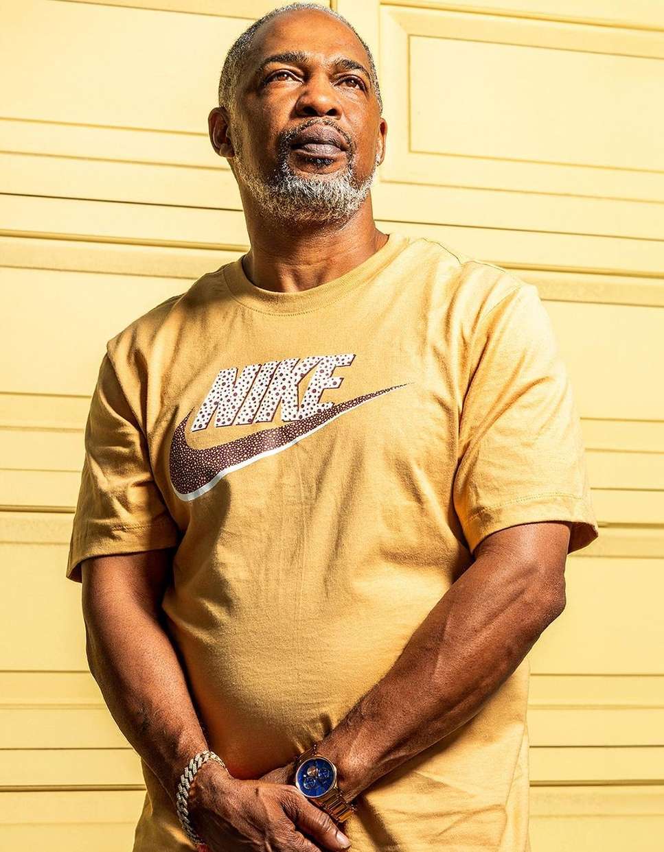 Close-up shot of a mature African-American man wearing a Nike T-shirt, with a light yellow wall in the background.