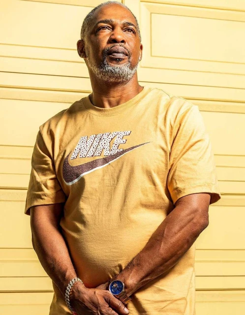 Close-up shot of a mature African-American man wearing a Nike T-shirt, with a light yellow wall in the background.