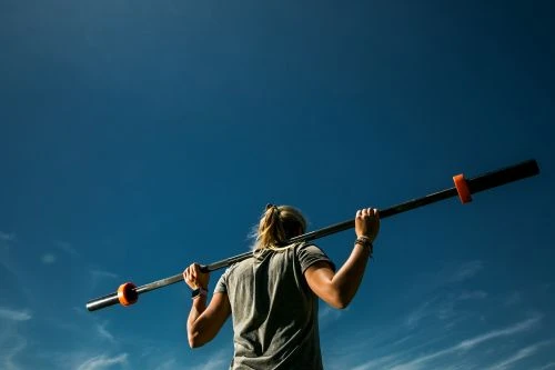 Woman exercises outdoors with a barbell against a bright blue sky. Strength training and fitness. Healthy lifestyle and exercise concepts.