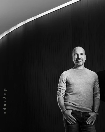 Portrait of a bald man with a beard wearing a knit sweater standing against a dark ribbed wall by Christie Hemm Klok