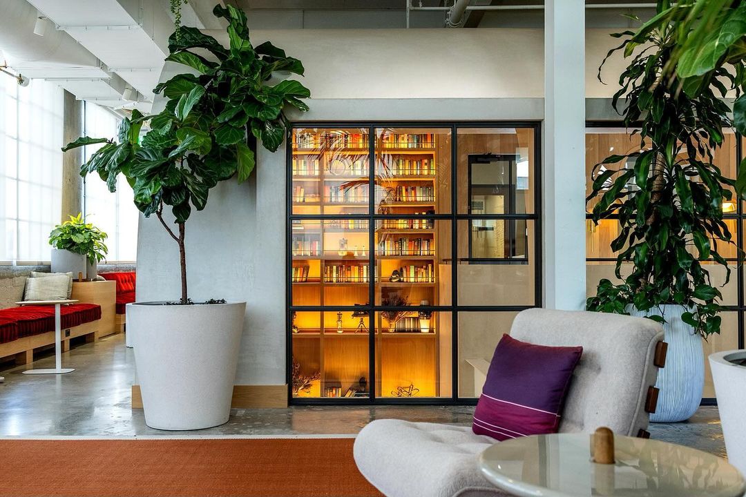 Modern indoor space featuring potted plants, cozy seating, a glass-enclosed bookcase, and contemporary design elements.