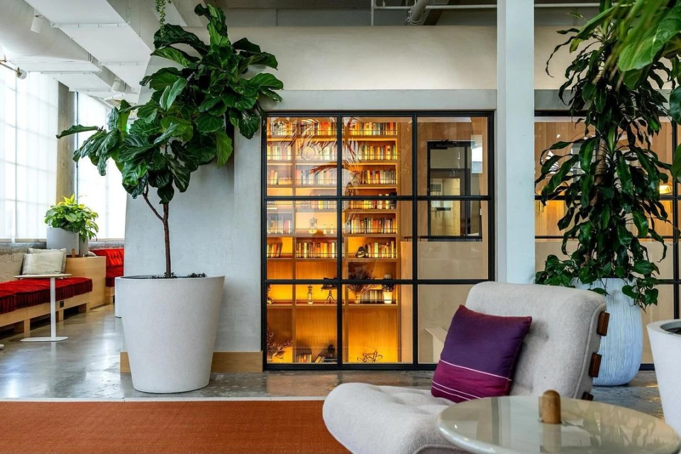Modern indoor space featuring potted plants, cozy seating, a glass-enclosed bookcase, and contemporary design elements.