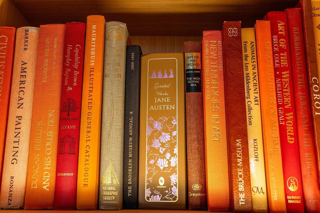 A shelf filled with colorful books of art, literature, and history, stacked tightly in a wooden bookshelf, creating a rich, textured display.