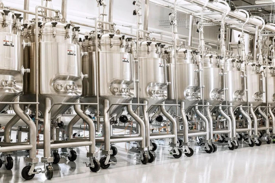 Stainless steel tanks on wheels dominate the interior of an industrial food processing facility, featuring metal piping and a clean, reflective floor.