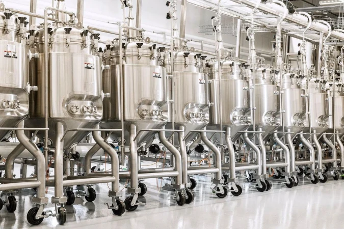 Stainless steel tanks on wheels dominate the interior of an industrial food processing facility, featuring metal piping and a clean, reflective floor.