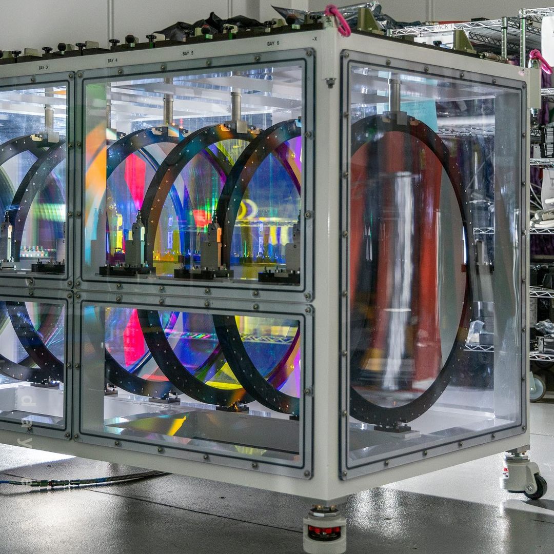 Complex transparent lab equipment with iridescent circular components and white frame on wheels, scientific research or industrial design.