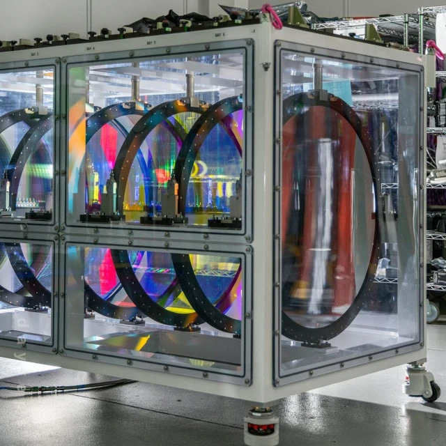 Complex transparent lab equipment with iridescent circular components and white frame on wheels, scientific research or industrial design.