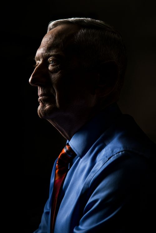 Older man portrait in profile against dark background. The man wears a blue dress shirt and colorful tie in a formal setting.