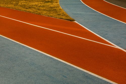 Orange and blue running track with white lane lines and grass in the background, creating a dynamic composition.