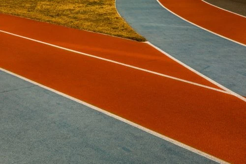 Orange and blue running track with white lane lines and grass in the background, creating a dynamic composition.