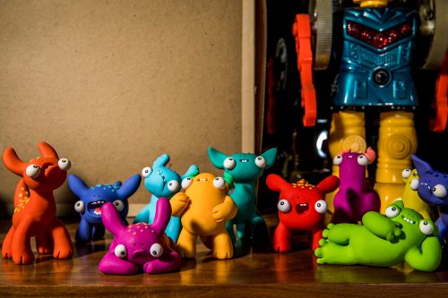 Colorful group of toy monsters in varying shades posing together on a brown wooden surface, with a toy robot in the background.