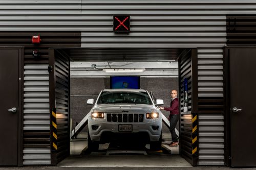 White Jeep SUV parked in a garage with a man standing near the open driver's side door, facing the camera in an indoor setting.