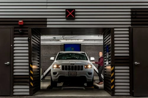 White Jeep SUV parked in a garage with a man standing near the open driver's side door, facing the camera in an indoor setting.