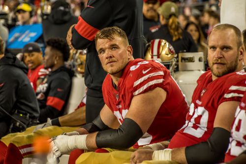 Football players in red jerseys sit on bench during game, showcasing team uniforms, stadium environment, and camaraderie among athletes.
