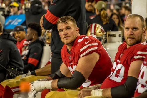 Football players in red jerseys sit on bench during game, showcasing team uniforms, stadium environment, and camaraderie among athletes.