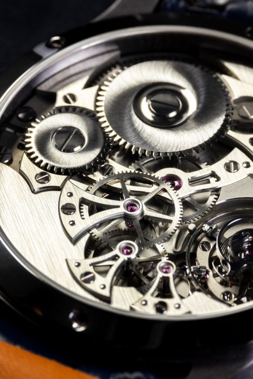 Close-up of the inner workings of a watch featuring intricate silver gears, screws, and ruby accents, all set against a dark background.