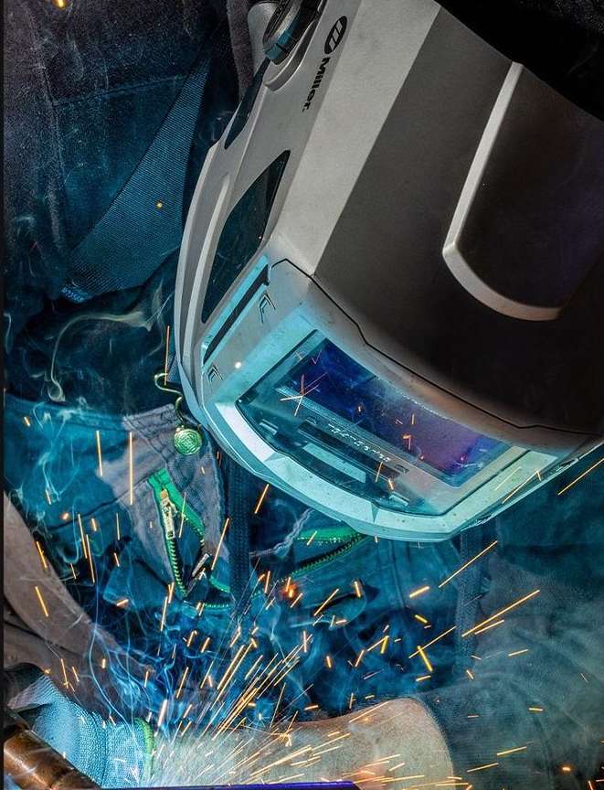 Welder wearing a protective mask, sparks flying, and smoke visible in a close-up shot showing work in progress.