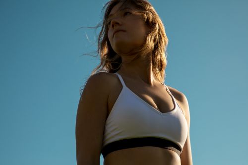 Low-angle shot of a woman with blonde hair in a white sports bra against a clear blue sky, photographed by Christie Hemm Klok.