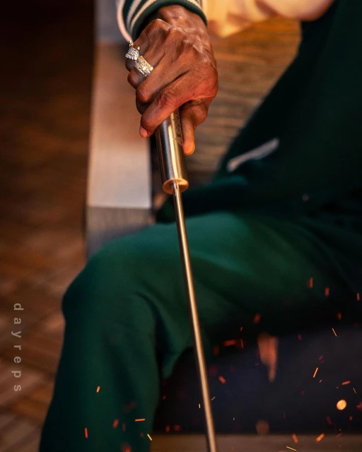 Close-up shot of an adult male's hand holding a gold metal skewer, showcasing a diamond ring, with a blurred background of sparks.