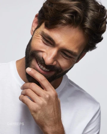 Close up portrait of a smiling bearded man in a white t shirt with hand near chin photographed by Baldomero Fernandez