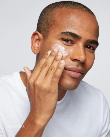 Close-up of a man applying skincare product to his face with his hand, showcasing beauty and grooming in a clean studio setting.