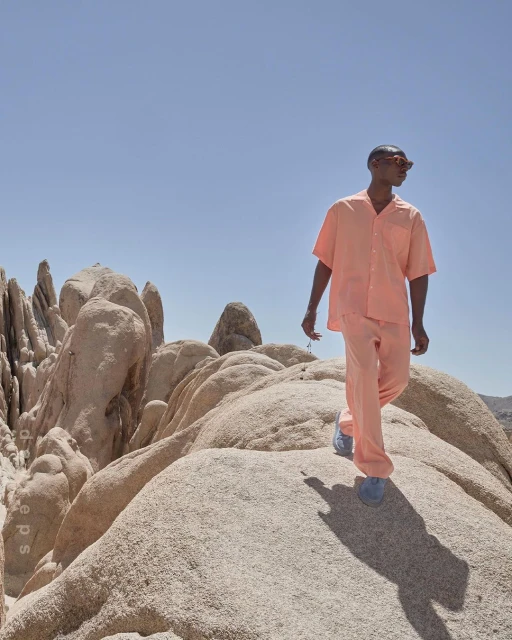 Man in matching peach shirt and pants walking in the desert on textured rocks under a clear sky in desert landscape setting.