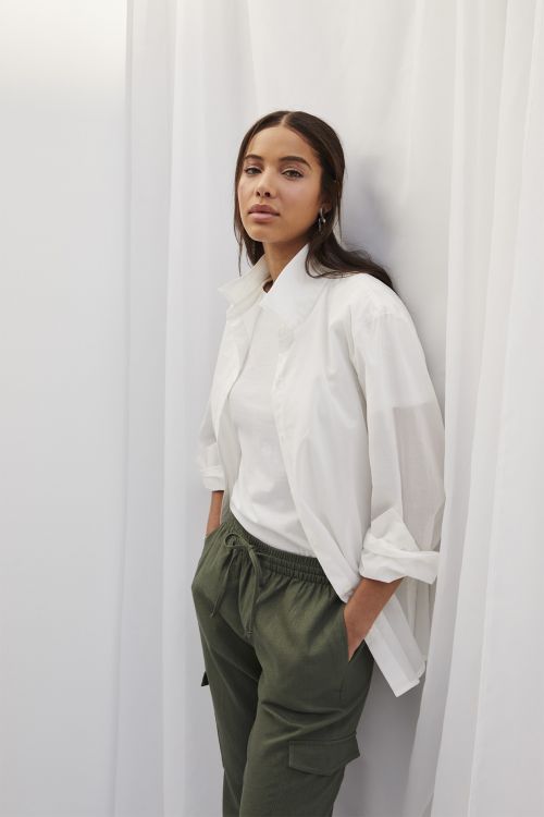 A woman poses in a white collared shirt and olive green cargo pants against a neutral background, offering a relaxed yet stylish look.