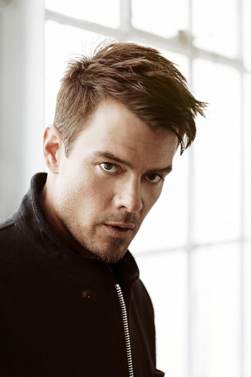 Portrait of a dark-haired adult male in a black jacket looking at the camera with a neutral facial expression indoors near a window.