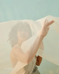 Woman with curly dark hair behind a sheer cream fabric held up by her outstretched arm