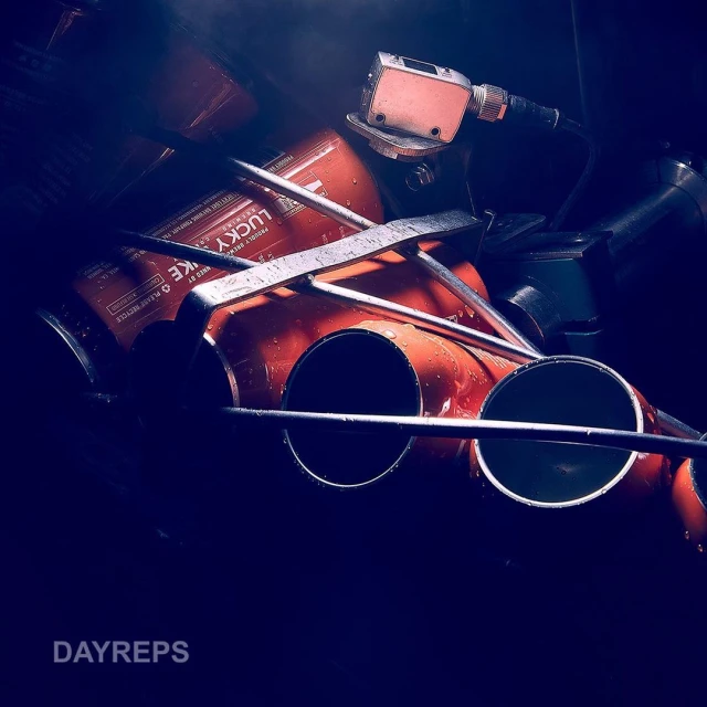 Close-up of stacked orange industrial metal pipes with steel supports in dim lighting. The scene captures a gritty, urban industrial aesthetic.
