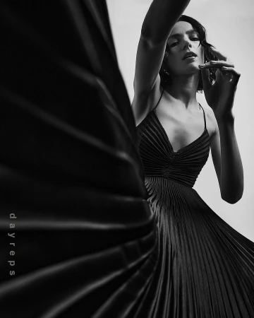 Model in a black pleated dress posing dynamically with dramatic lighting in a monochrome fashion photograph.