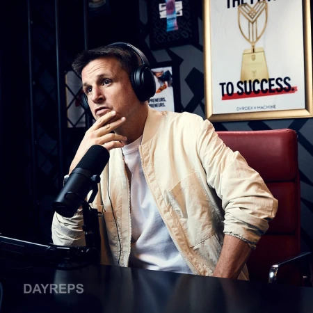 Man wearing headphones sits in a red chair with a microphone. Photo studio setting with promotional poster on the wall.