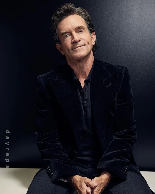Portrait of an adult male with dark hair wearing a black velvet jacket, seated against a dark background in a photo studio setting.